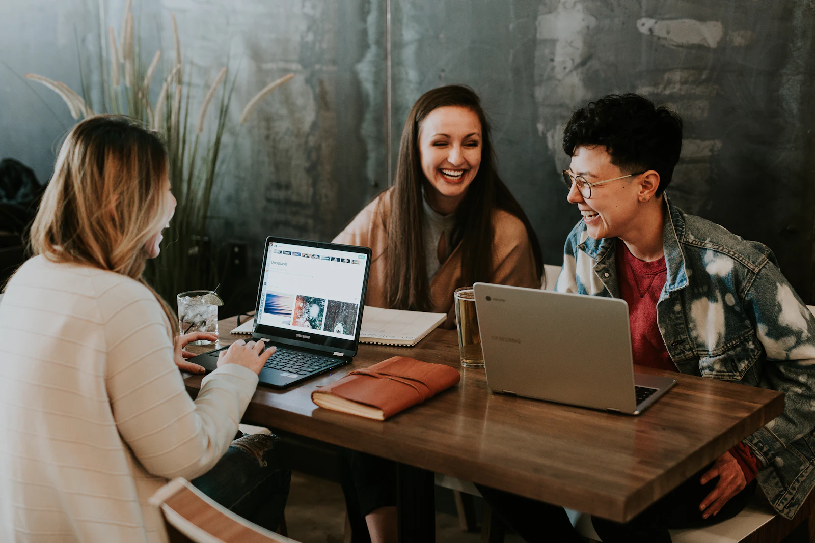 Drie collega's werken lachend samen aan laptops